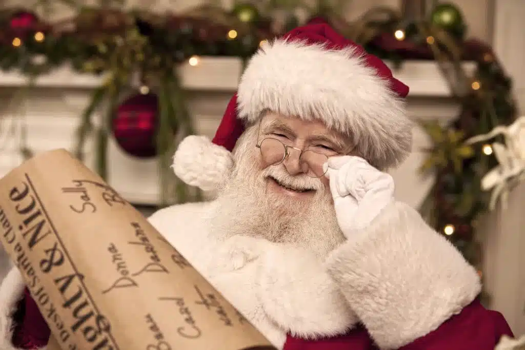 Santa holding his eyeglasses close to his eyes while checking the naughty and nice list.