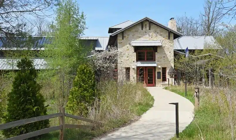 Front entrance of Schlitz Audubon Nature Center surrounded by native grasses and spring trees.