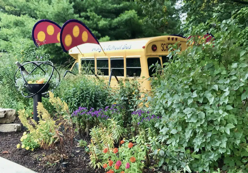 Magic School Bus display surrounded by lush plants at Bookworm Gardens.
