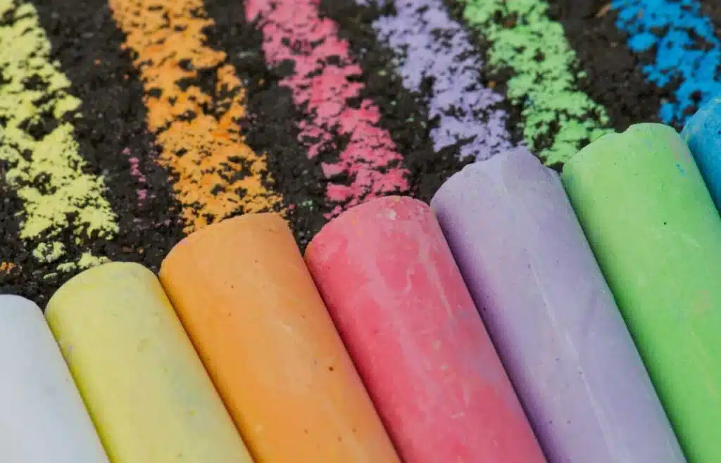 Six large pieces of sidewalk chalk in bright and vibrant yellow, orange, pink, purple, green and blue.