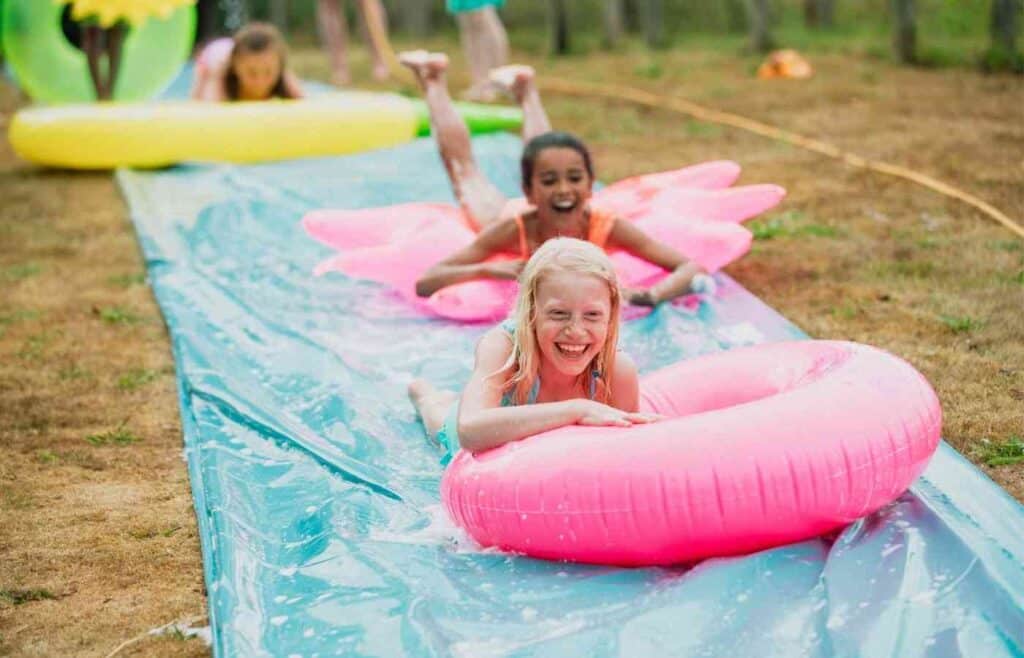 Three girls on inflatable rings playing slip n slide on wet blue mat