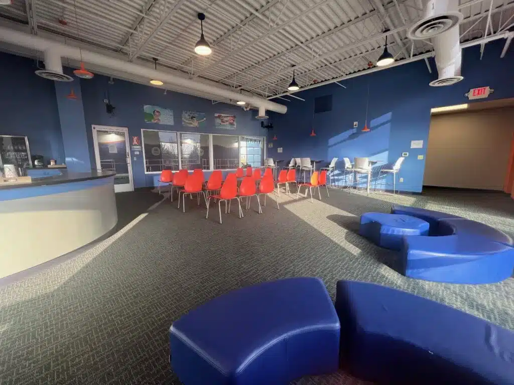 Parent viewing room with chairs, tables, and large windows overlooking the pool. 