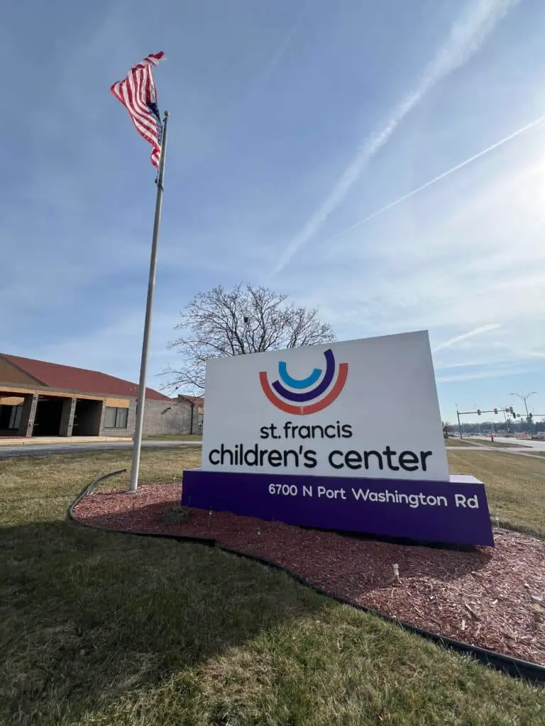 The ground sign of St. Francis Children's Center in Port Washington Road Milwuakee beside the American flag