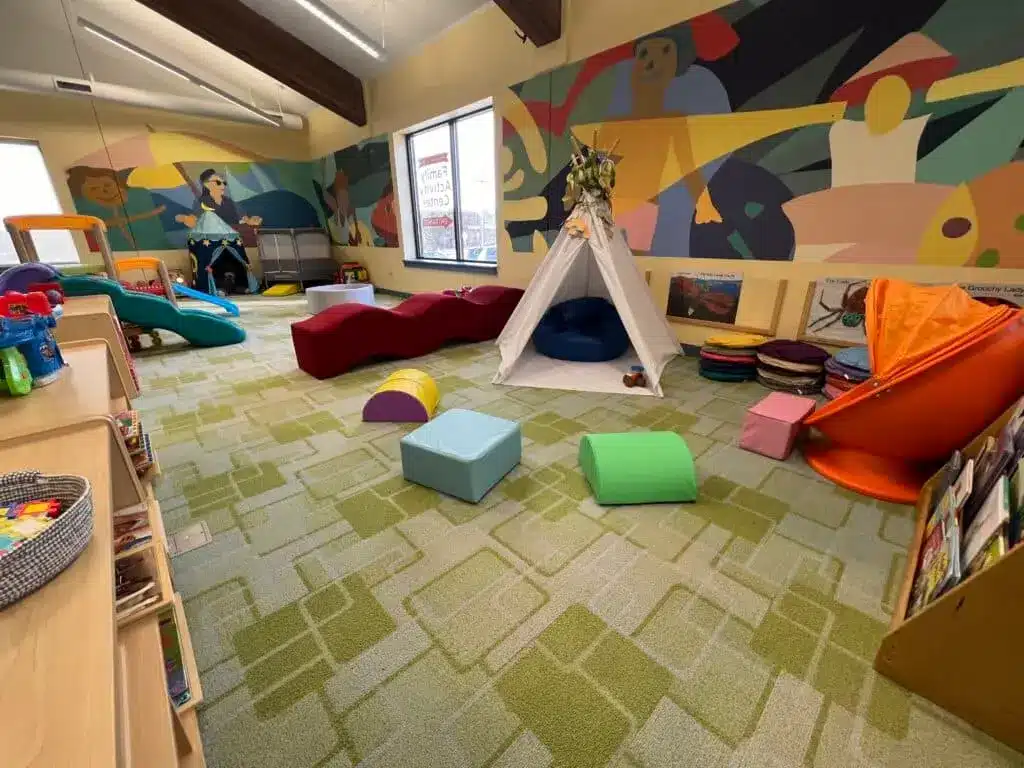 Colorful slides and chairs with large blocks and a white children's teepee and wall murals 