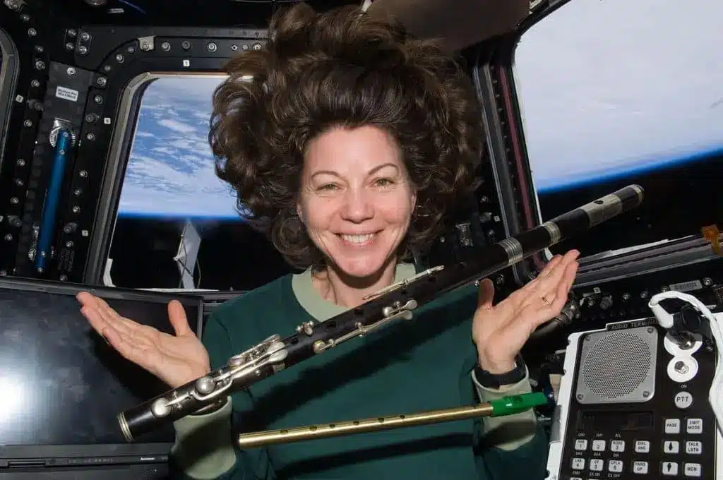 An astronaut grinning and showing floating musical instruments in outer space