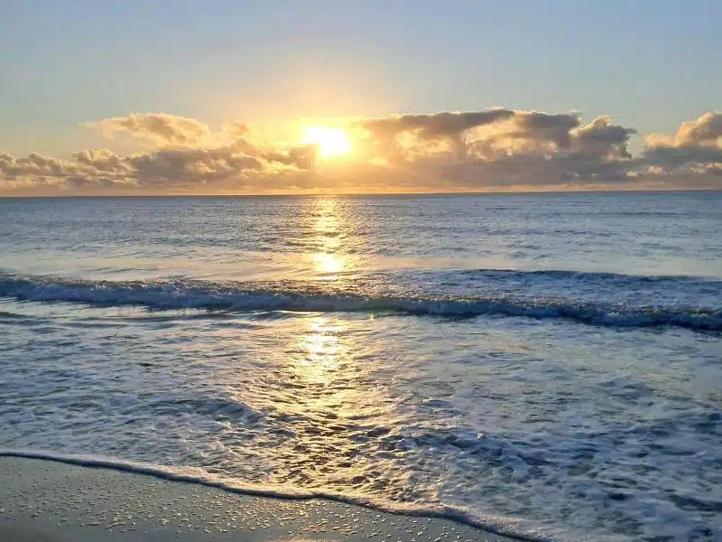 Sunrise breaking through clouds over a peaceful ocean horizon.