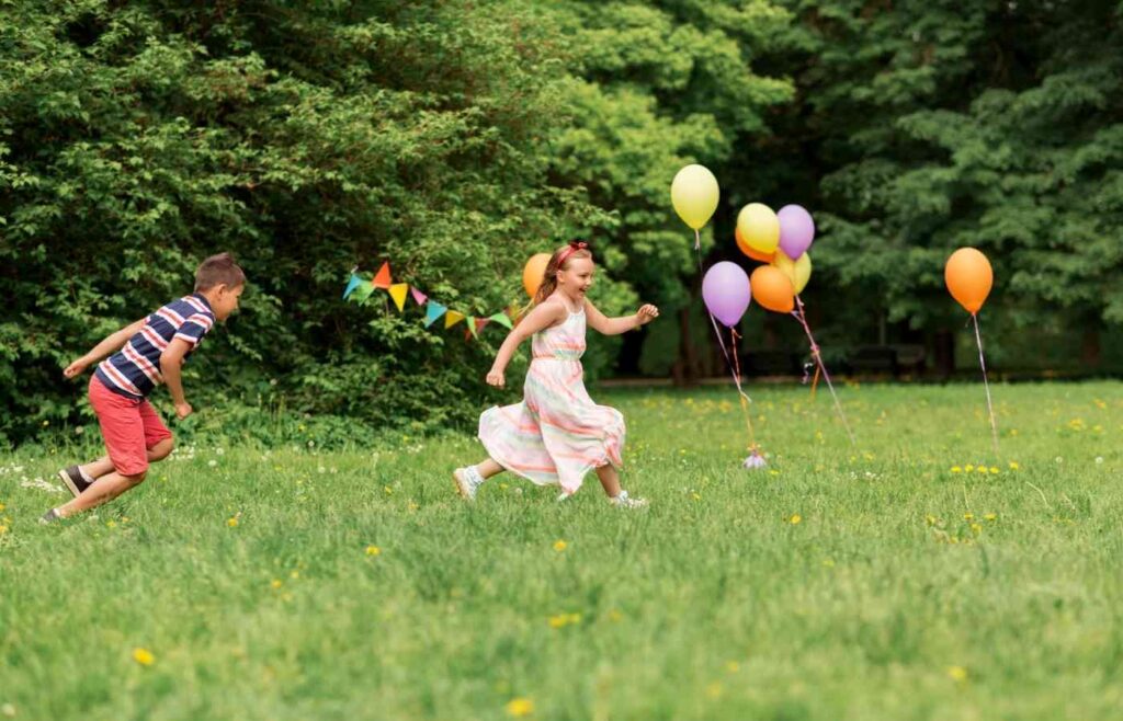 Two kids prunning during an outdoor birthday party with balloons
