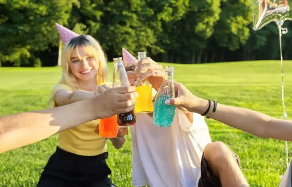 Teens clinking colorful drinks at an outdoor birthday party celebration