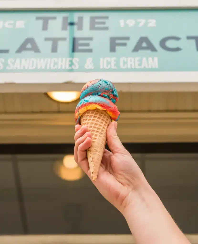 A person holding a multicolored ice cream in front of The Chocolated Factory