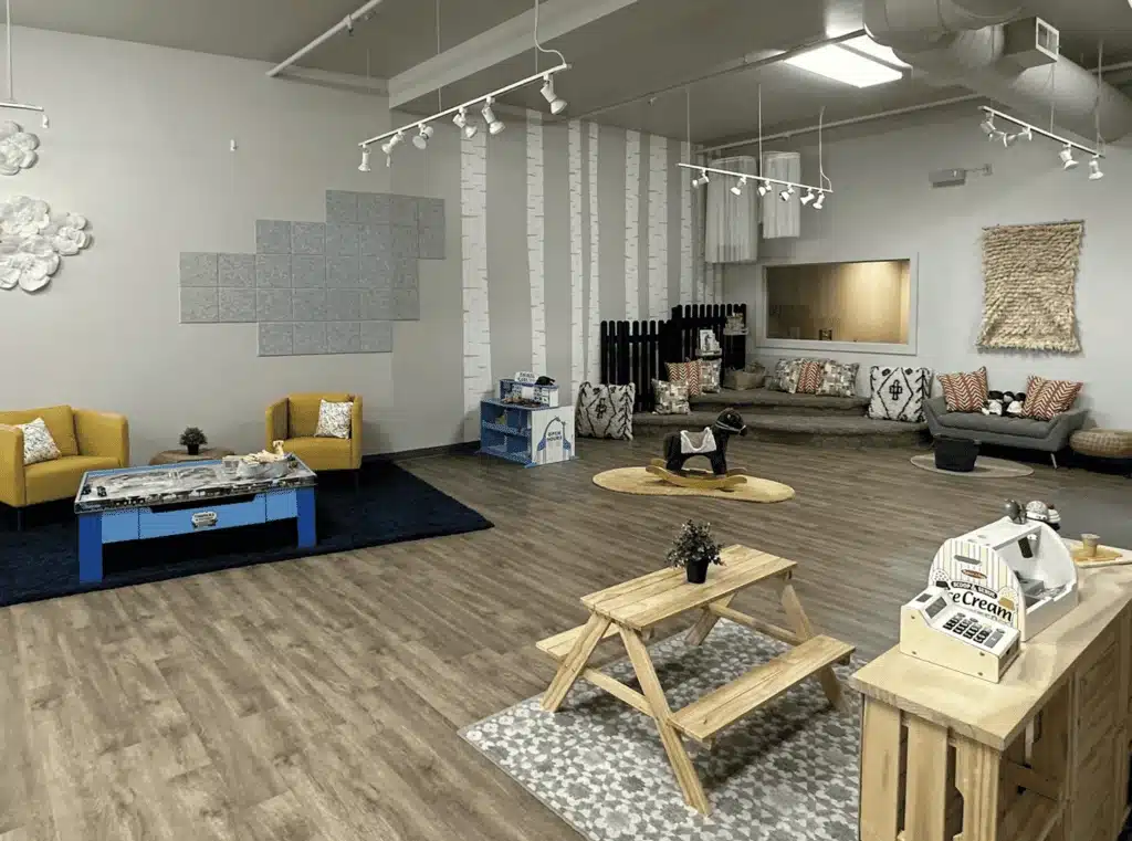 Interior of The Play Retreat with yellow pretend living playsets, wooden lunch tables and murals on white walls.