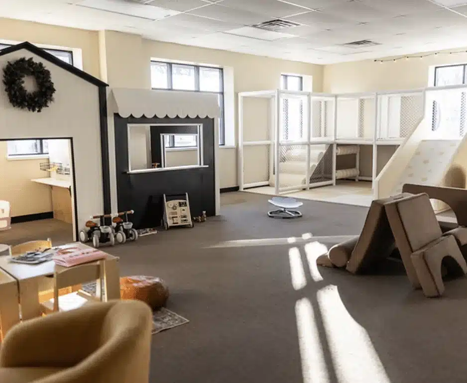 Indoor play area with yellow lounge chair, pallet tables with cream walls and grey carpeting
