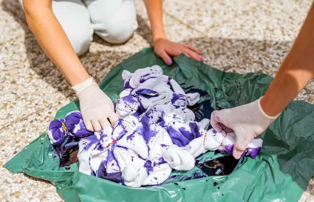 Children wearing gloves dyeing bundled white shirts with purple dye 