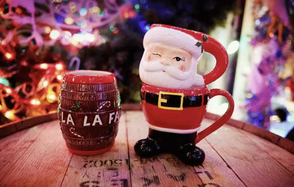 Santa-shaped mug with a twinking eye stands on the right and barrel style mug with text saying LA LA Fa