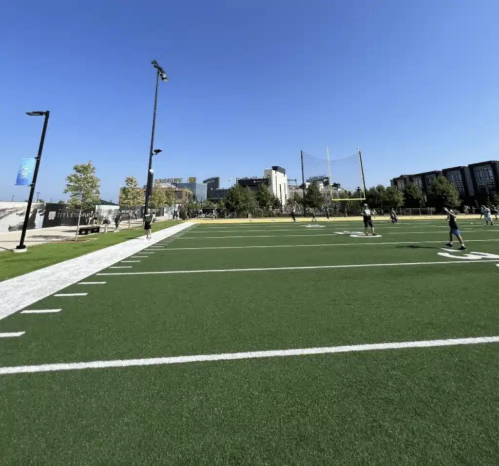 Coaches and players practicing football at a field while a person is running in the tracks