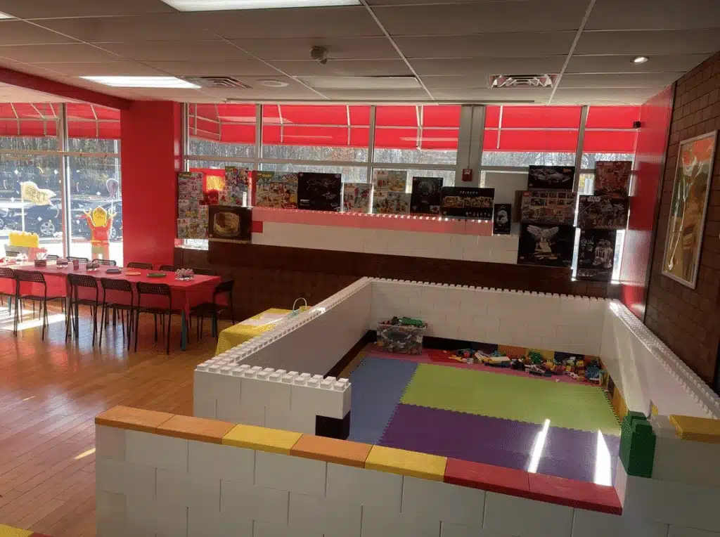 Large Lego pieces serving as play area and red long tables with brown chairs at Tosa Block Party.