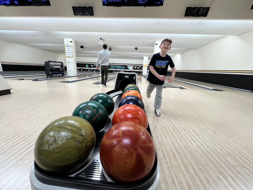 A little boy in black shirt getting a ball for another round of bowling 