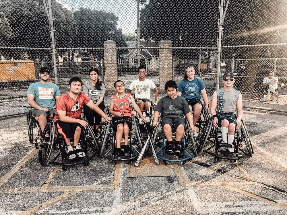 Eight people sitting on their wheel chairs and two of them are holding baseball bats