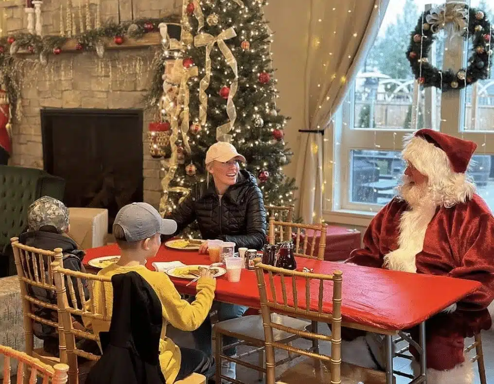 Santa talking to a mother in black leather jacket and two kids who are eating pancakes and omelette.