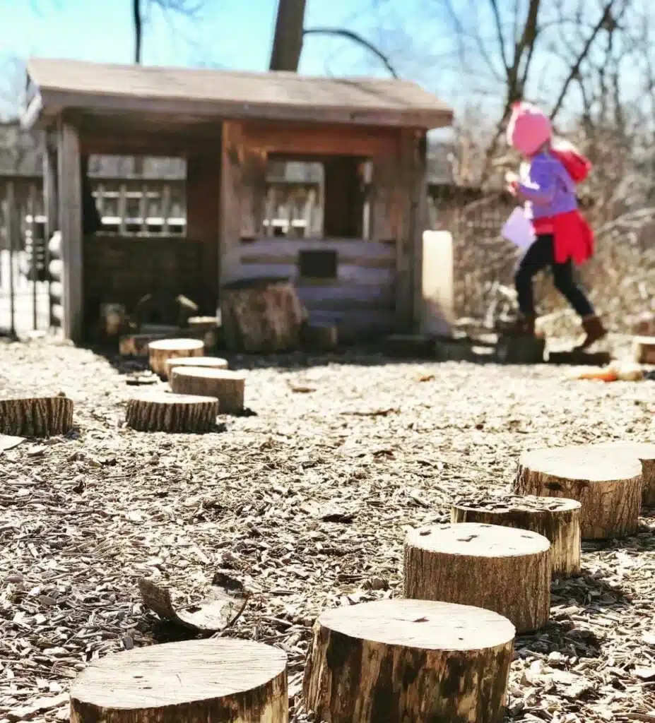 Child walking on log stepping stones in Wehr Nature Center’s nature play area.