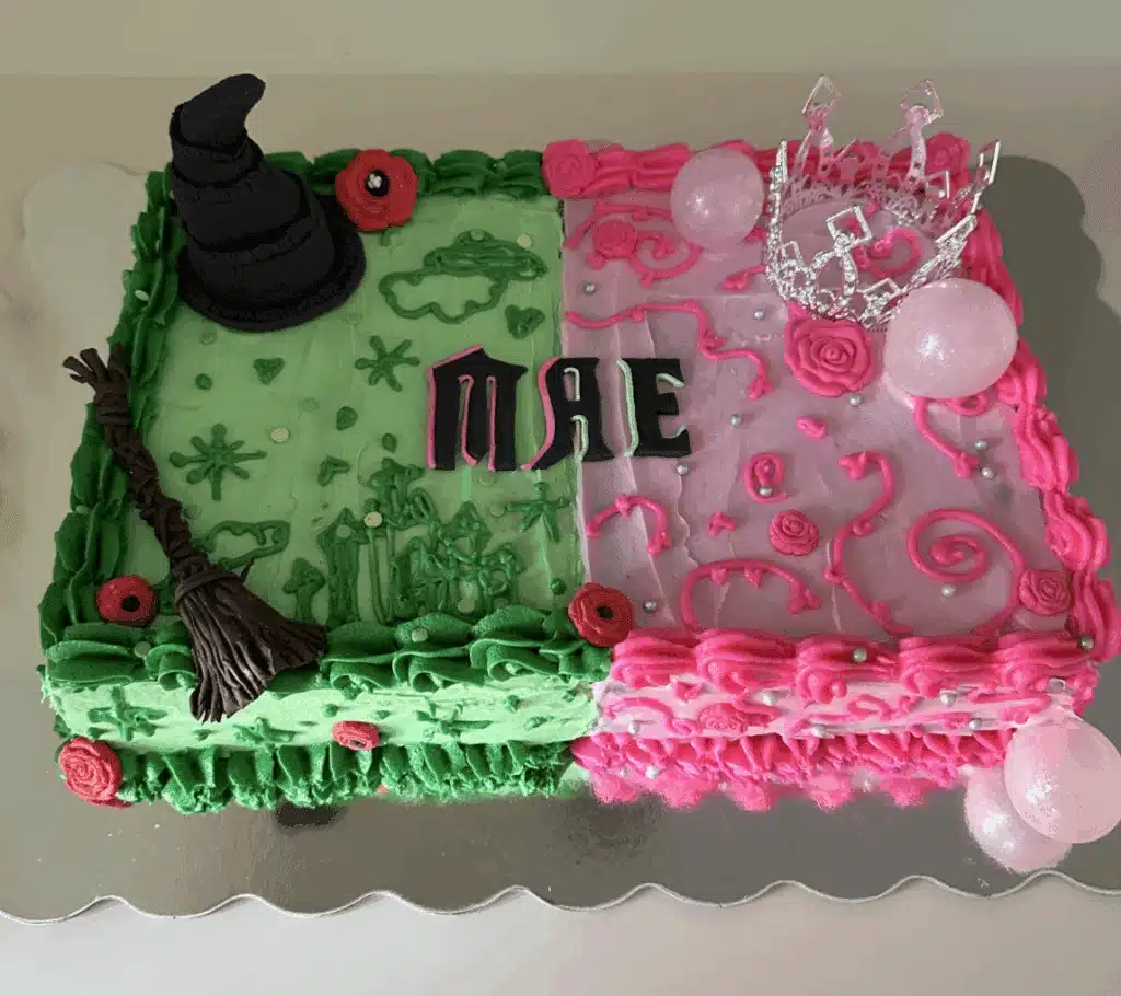 Aerial view of wicked themed cake, one half green with a witch's hat and broom, and the other half pink with balloon bubbles and a silver crown.
