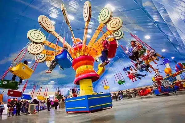 Children ride colorful indoor swings under a bright, sky-themed ceiling.