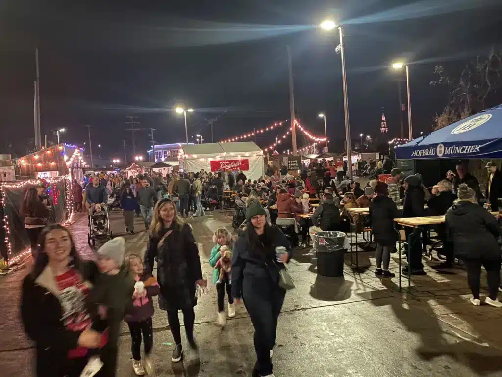 People eating and strolling at a holiday market with some bringing this toddlers to enjoy the festivities